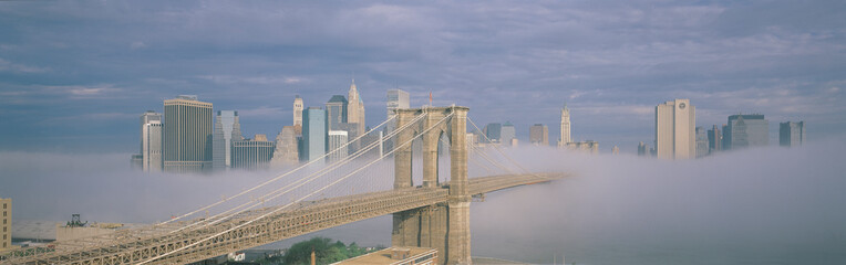 New York City, New York shows Brooklyn Bridge with fog under neath it