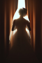 Beautiful bride standing near window. The girl in a white wedding dress.