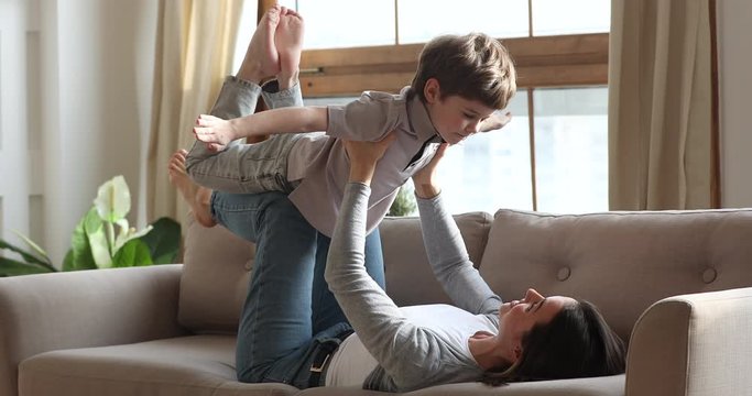 Funny boy preschooler playing plane game with mother on couch