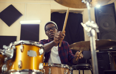 Portrait of young African-American drummer preparing for concert or rehearsal during sound check,...