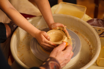 A close-up of the hand of a male potter who teaches his pupil, a child of the art of making a pot or a vase of clay. People working on potters.