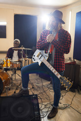 Obraz premium Full length portrait of contemporary long-haired man singing to microphone during rehearsal or concert with music band in background