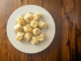 Portion of traditional Russian dumplings on a white plate and wooden table, Top view.