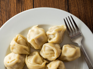 Portion of traditional Russian cooked dumplings on a white plate with metal fork on wooden table,
