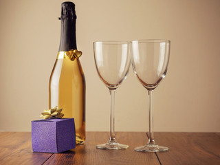 Two golden hearts with glitter on a bottle of sparkling wine and two empty glasses and blue gift box, Concept Saint valentine or romantic event.