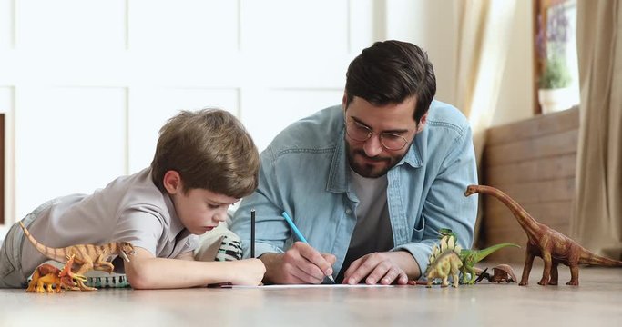 Caring father playing with child son drawing lying on floor