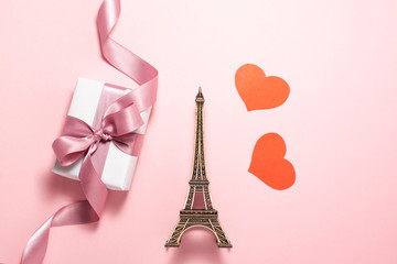 The Eiffel Tower, two red hearts and white gift box with purple ribbon bow on bright pink background. Flat lay top view of important sights of Paris. Romantic, Valentines day and travellings concept