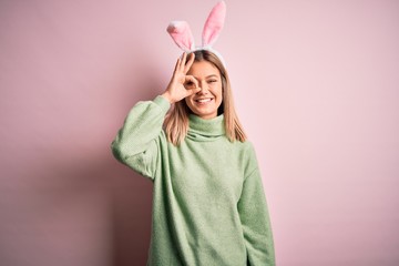 Young beautiful woman wearing easter rabbit ears standing over isolated pink background doing ok gesture with hand smiling, eye looking through fingers with happy face.