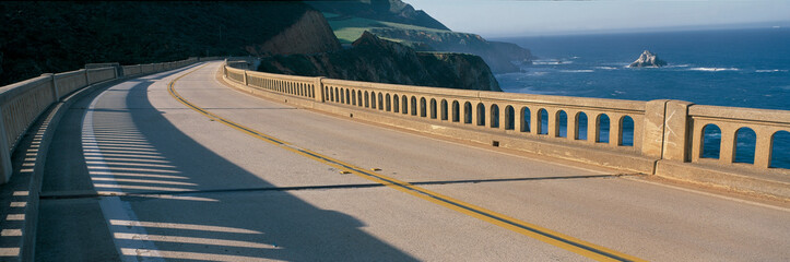 This is the road on the Bixby Bridge. It is Route 1, also known as Pacific Coast Highway. It is next to the mountainous coast and the Pacific Ocean. The road curves around to the right. © spiritofamerica