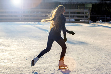 Girl with long hair skates on an ice rink in the sunlight and glare. Sport and hobbies. Holidays...