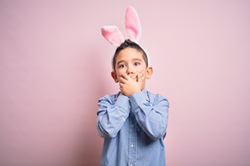 Young little boy kid wearing easter bunny ears over isolated pink background shocked covering mouth with hands for mistake. Secret concept.