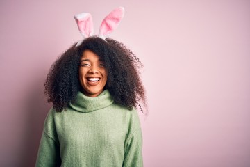 Young african american woman with afro hair wearing easter rabbit ears costume over pink background...
