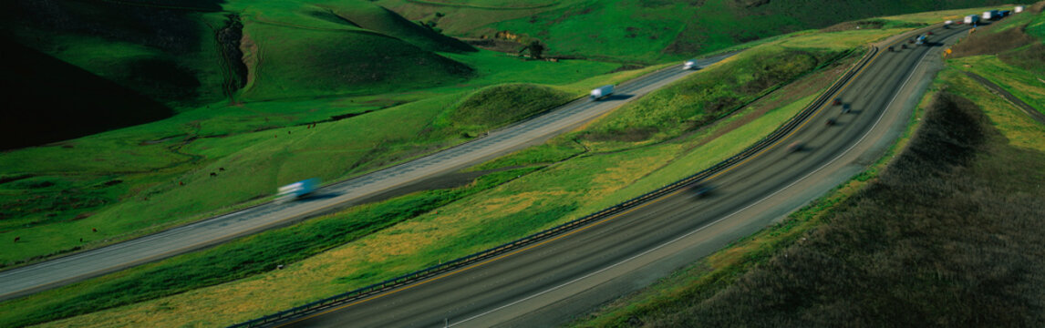 This is Route 580 at the Altamont Pass. There is green grass on each side of the highway with two separate roads for cars to travel in each direction.
