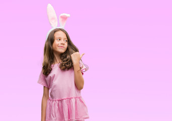 Obraz na płótnie Canvas Brunette hispanic girl wearing easter rabbit ears pointing and showing with thumb up to the side with happy face smiling