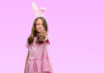Obraz na płótnie Canvas Brunette hispanic girl wearing easter rabbit ears with open hand doing stop sign with serious and confident expression, defense gesture