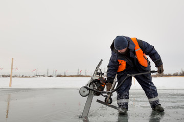 Worker cuts out ice blocks in size on the ice of a frozen lake