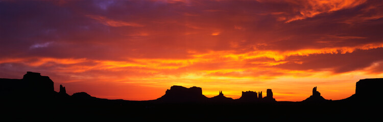 This is sunrise on Monument Valley. The rocks are in silhouette against an orange sky.