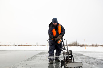 Worker cuts out ice blocks in size on the ice of a frozen lake