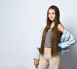 Teenage girl in striped t-shirt, denim jacket and pants. She looking at you, posing isolated on white studio background. Close up