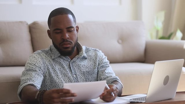 Focused african ethnicity businessman working remotely on computer.