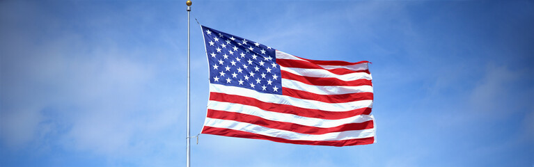 This is a shot of an American flag on a flagpole, waving in the wind against a blue sky.
