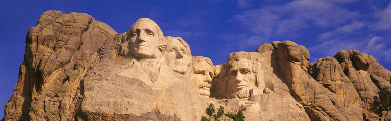 This is a close up view of Mount Rushmore National Monument against a blue sky. It shows the four faces of George Washington, Thomas Jefferson, Theodore Roosevelt, and Abraham Lincoln. - obrazy, fototapety, plakaty