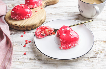 Pink mousse cakes in the shape of a heart decorated with mini hearts on a white rustic background. Heart shaped cakes for Valentine's Day or Mother's day. Selective focus.