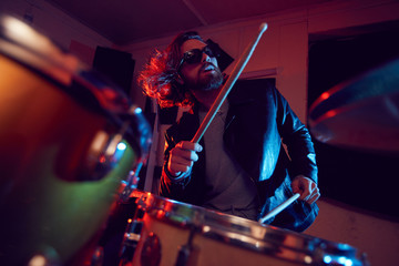 Low angle portrait of handsome young man rocking drums during music concert in bright lights, copy...