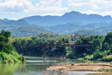 Fototapeta premium Scenic View of the Nam Khan River in Luang Prabang Laos with Hazy Cloudy Mountains in the Background