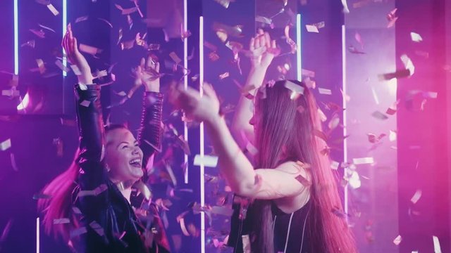 Neon women. Girls night. Amused teen friends having fun in shiny confetti rain pink glow.