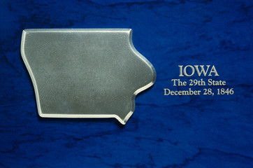 This is a silver map of the state of Iowa. It is set against a blue background. It reads Iowa, the...