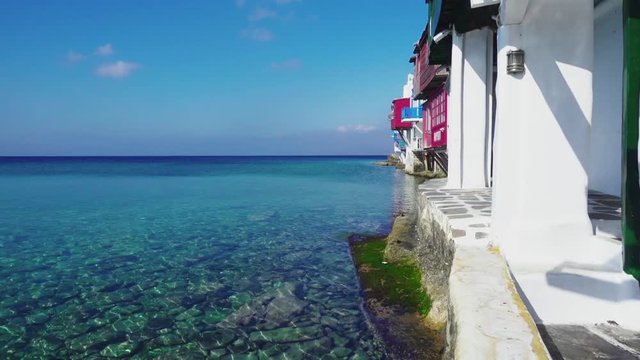 Sliding view showing shallow water and pebbles underwater along the houses at the waterfront of Little Venice in Mykonos old town, Greece