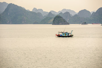 Obraz premium Traditional Vietnamese Fishing Boat Surrounded by Karst Mountains in Bai Tu Long Bay in Halong Bay Vietnam on a Cloudy Day