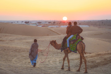 Tourists riding camel on Thar desert in Jaisalmer during the sunset, India. Thar Desert is a large...