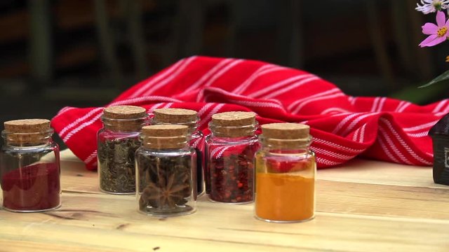 Table with cork topped jars of spices with plate of baklava and small vase with flowers. slow pan right 