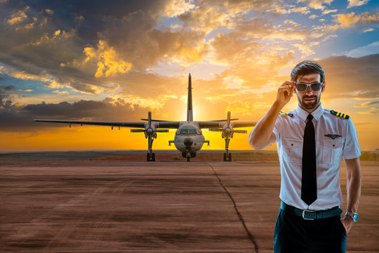 Portrait handsome pilot man in uniform waring sunglasses posing with airplane sunligh tray background. 