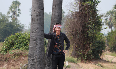 Agriculturist male with loincloth wrapped over the head, his hand on sugar palm and.standing on nature.