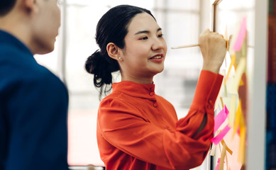 Casual business woman planning and brainstorm writing over the project with stickers note on glass window at modern office.Teamwork concept