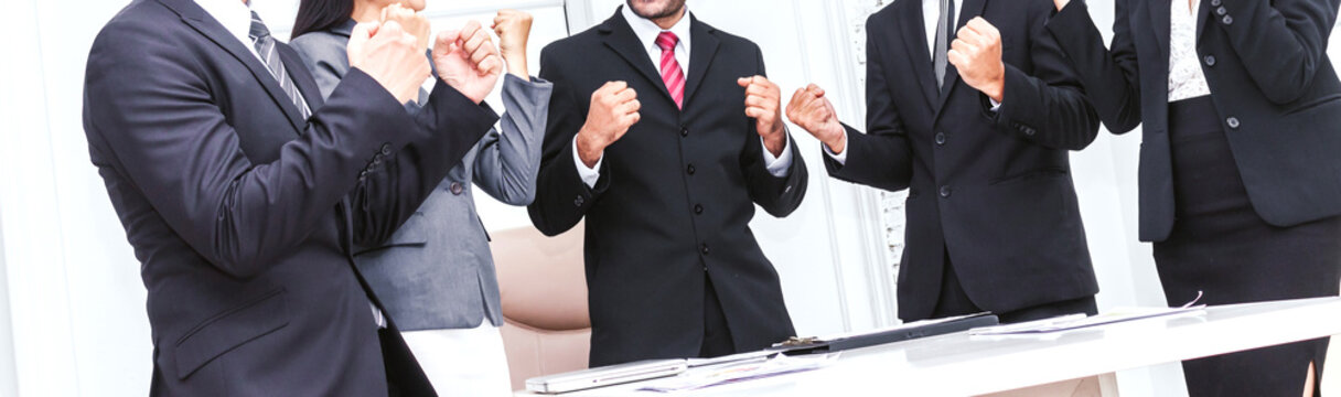 Successful group of business people team in elegant suit celebrating with arms up in office