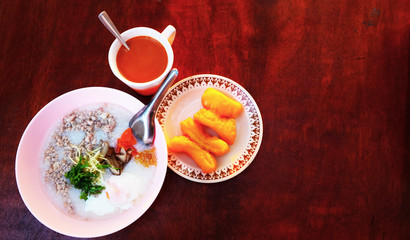 rice porridge pork with fried stick and a cup of Thai hot milk tea on wooden table for breakfast.