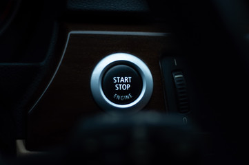 Engine start stop button of a modern car in dark cool colors.
