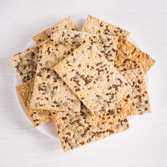 crispy wheat cakes with sesame, flax and sunflower seeds on plate on white wooden background. vegetarian food, eco food concepts