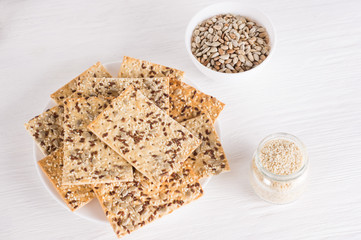 crispy wheat cakes with sesame, flax and sunflower seeds on plate on white wooden background,  sesame seeds in a jar. vegetarian food, eco food concepts