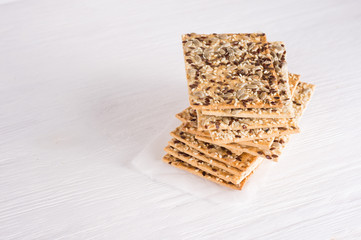 Stack of crispy wheat cakes with sesame, flax and sunflower seeds on on a napkin on white wooden...
