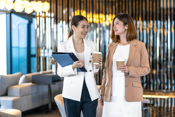 Two asian businesswomen talking during coffee break in modern office or coworking space, coffee break, relaxing and talking after working time, business and people partnership concept