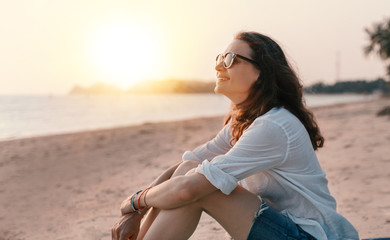 Young beautiful woman in sunglasses enjoying a summer day on the beach at sunset on a sandy beach...