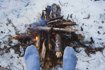 Man's legs against the bonfire in the forest. Bushcraft symbol. Solo survival in nature. Winter in the forest, travel