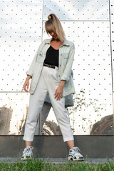 beautiful caucasian girl in fashionable colored sneakers, light jeans and a jacket with a hairstyle tail posing cool on the street near a sparkling metal wall. Creative Posing Lessons for Girls