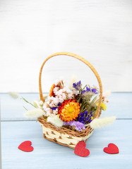 Fototapeta na wymiar A basket of dried flowers and red hearts on a blue tabletop