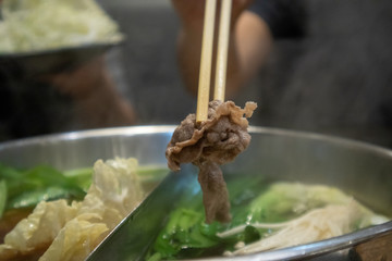 Close up of chopsticks picking up pork from hotpot.